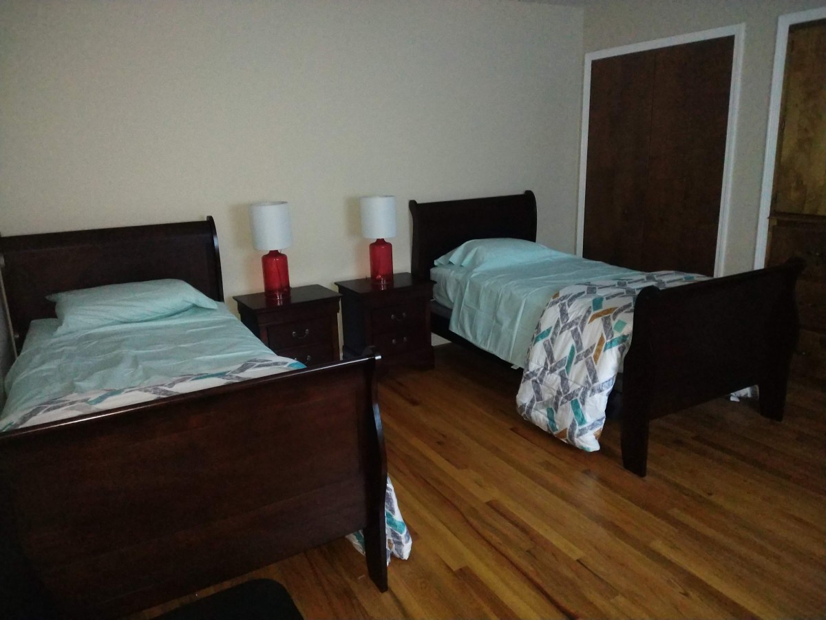 A cozy bedroom featuring twin beds with matching lamps on a nightstand and a hardwood floor.