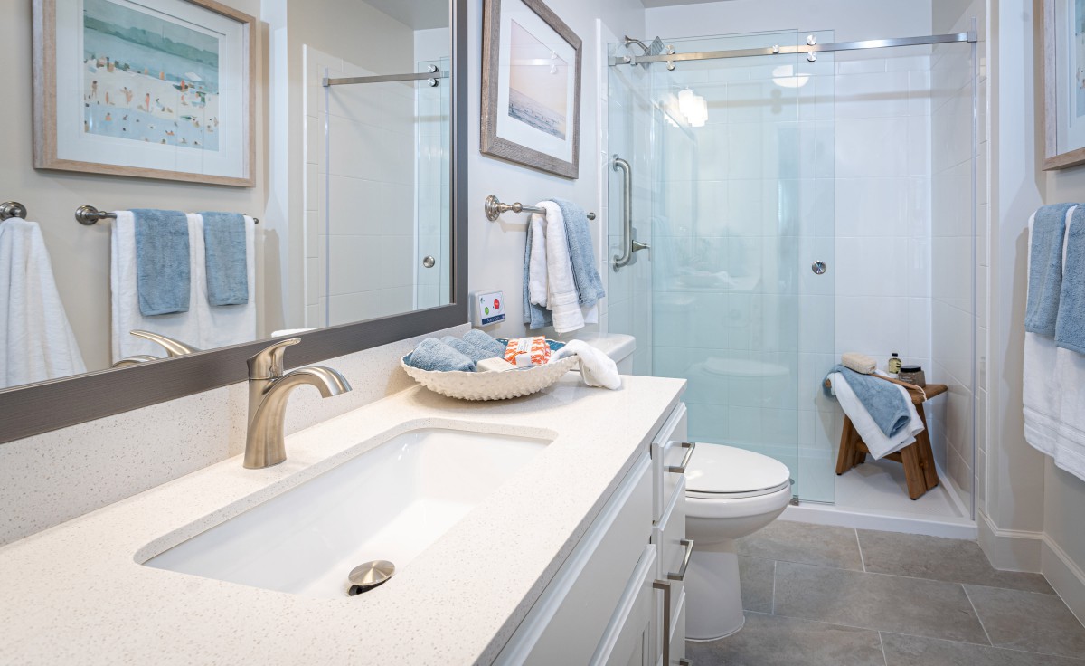 A modern, well-lit bathroom with a sleek design featuring a large mirror, countertop sink, and glass shower enclosure.