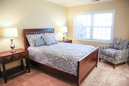 A cozy bedroom featuring a wooden bed with patterned bedding, a bedside lamp, and a large window letting in natural light.