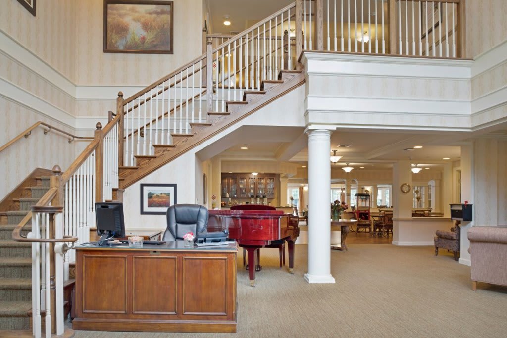 A spacious lobby with a wooden staircase, reception desk, and a grand piano.