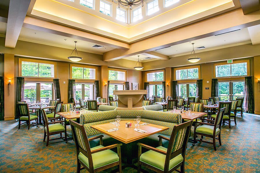 A spacious and well-lit dining area featuring neatly arranged tables and chairs, surrounded by large windows.