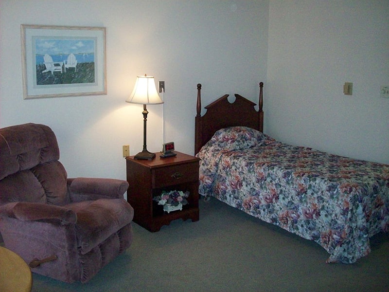 A cozy bedroom with a single bed, nightstand, and a plush chair.