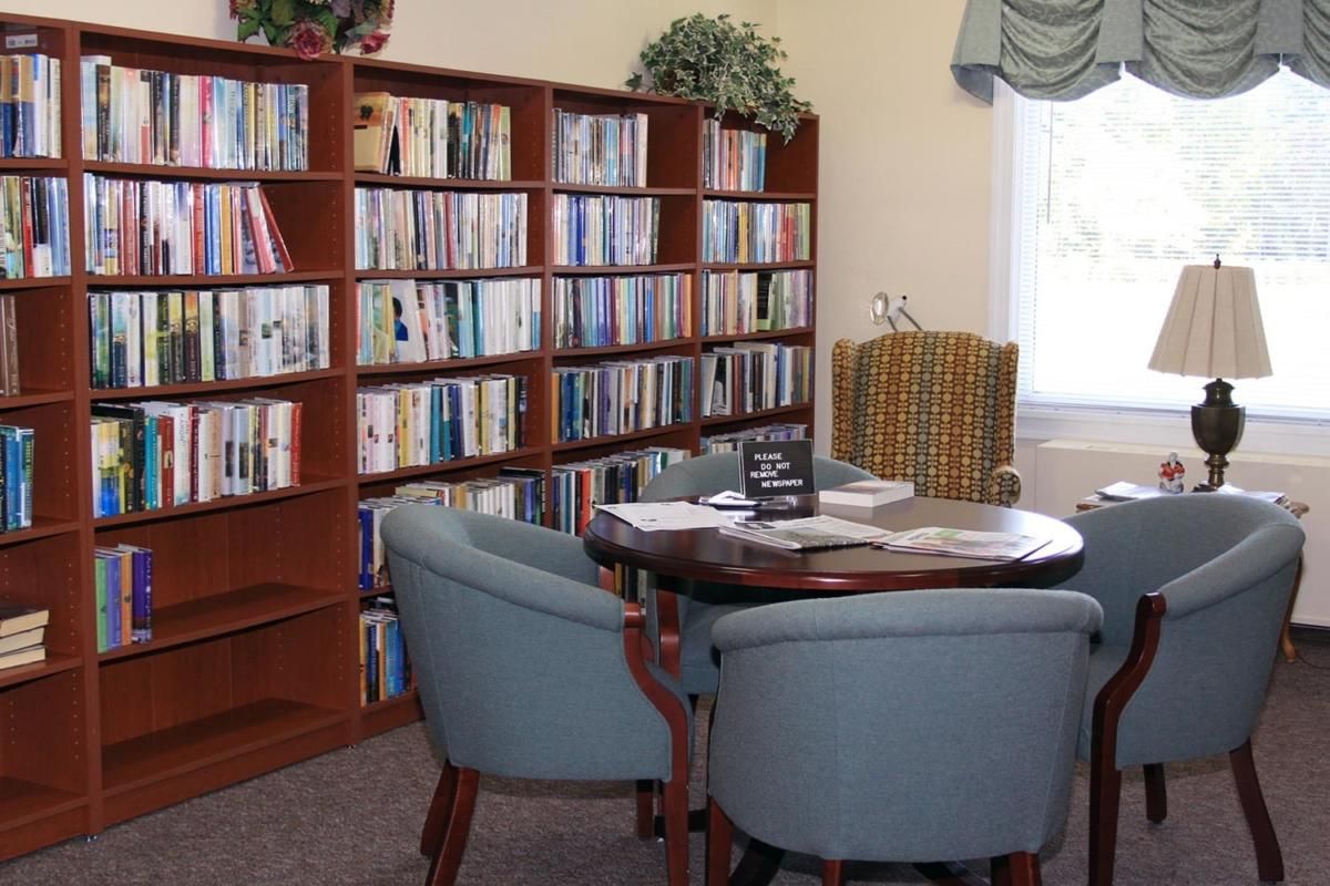 A cozy library reading area with bookshelves, a table, and chairs by a window.