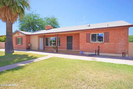 A charming single-story brick house with a well-maintained front yard under a clear blue sky.