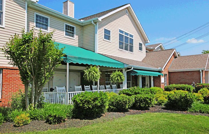 A residential house with a green awning and a well-maintained garden on a sunny day.