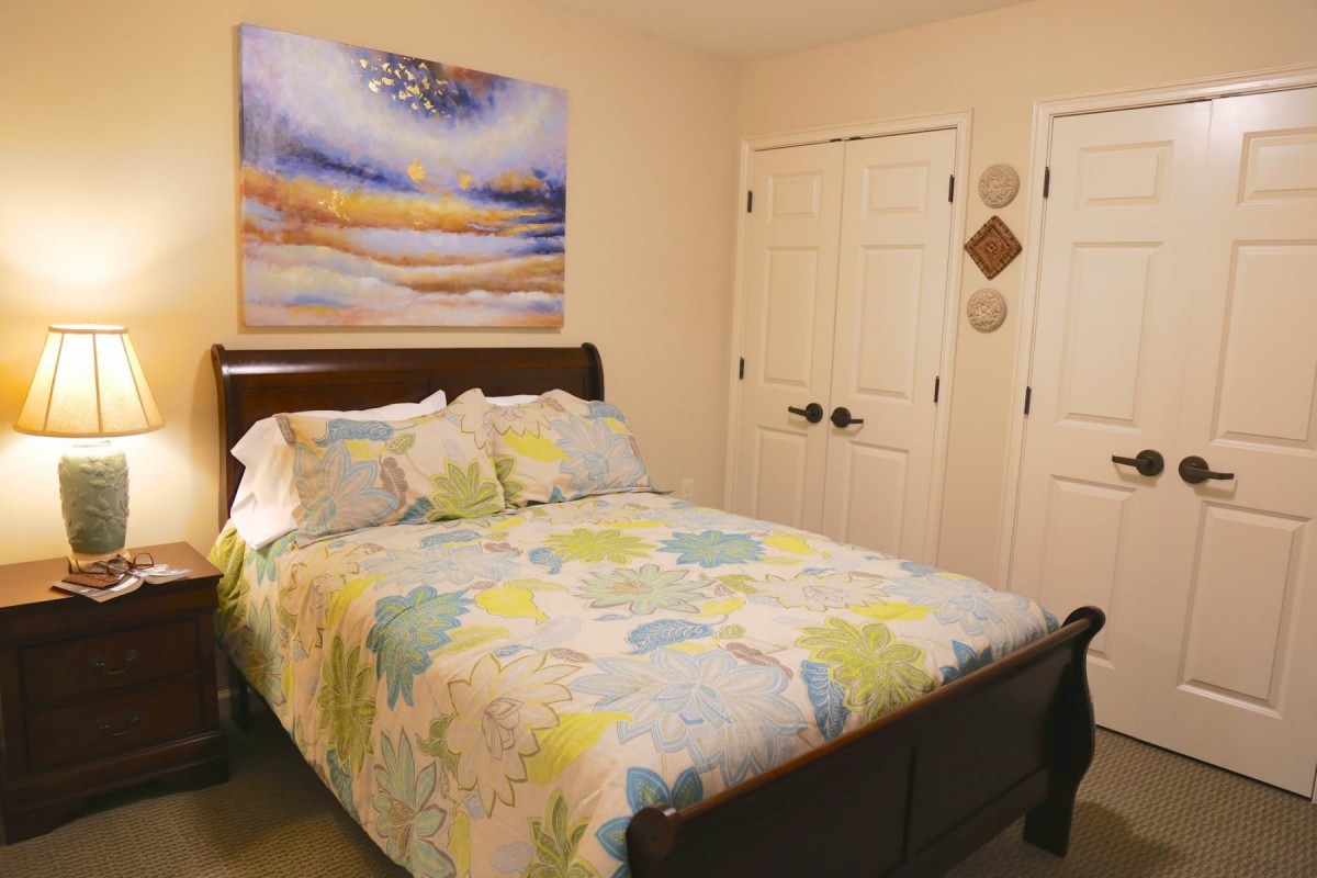 A cozy bedroom with a floral-patterned bedspread and artwork above the bed.