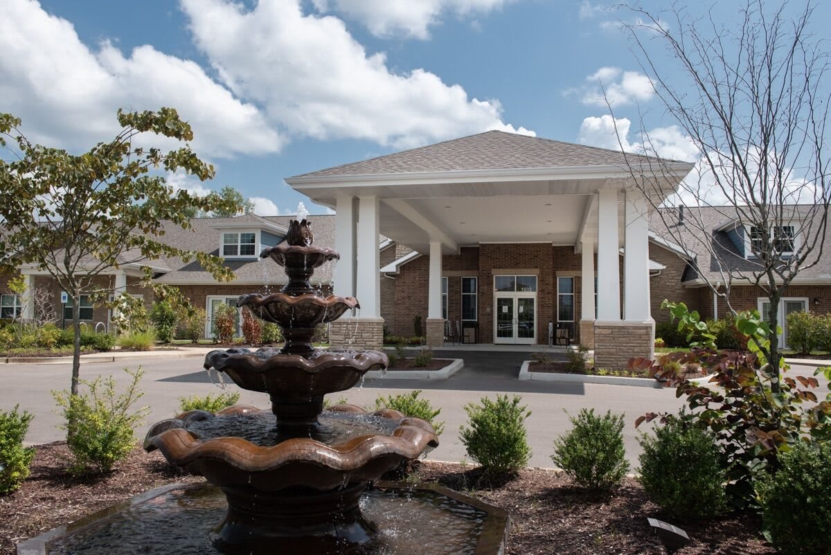 A building entrance with a decorative fountain in the foreground under a partly cloudy sky.