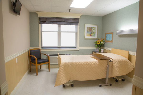 An empty hospital room with a neatly made bed and a sunny window.