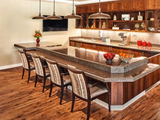 A modern kitchen with a large island and bar stools, featuring wooden cabinets and pendant lighting.