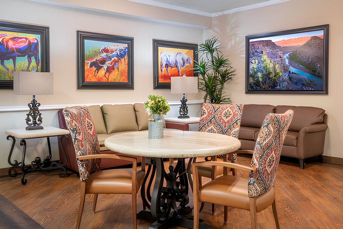 A cozy living room featuring a round table with patterned chairs, a comfortable sofa, and colorful artwork on the walls.
