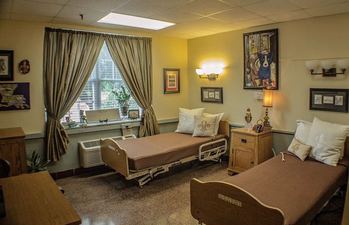 A well-lit hospital room with two patient beds, a window with curtains, and warm decor.