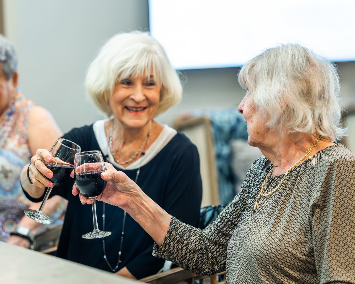 Two elderly women enjoying a glass of wine together.