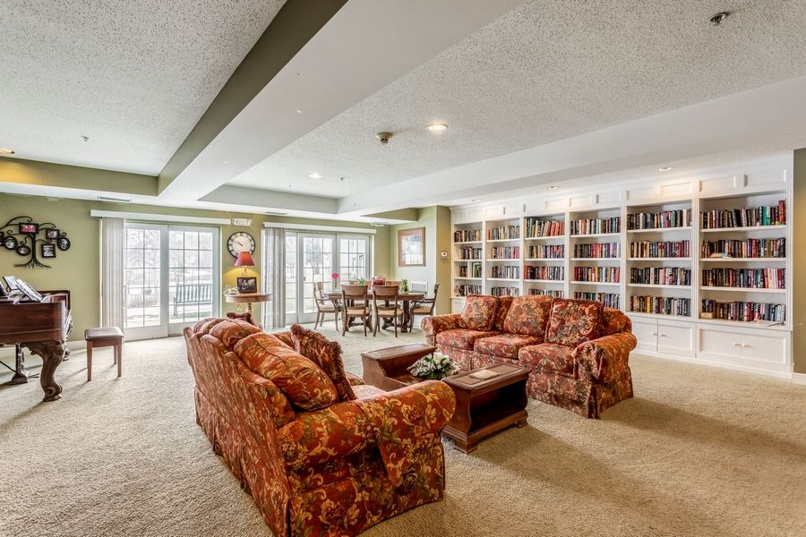 A spacious living room with floral sofas and extensive bookshelves, featuring a cozy dining area by large windows.