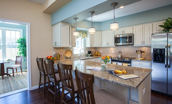A modern kitchen interior with granite countertops, bar stools, and pendant lighting.