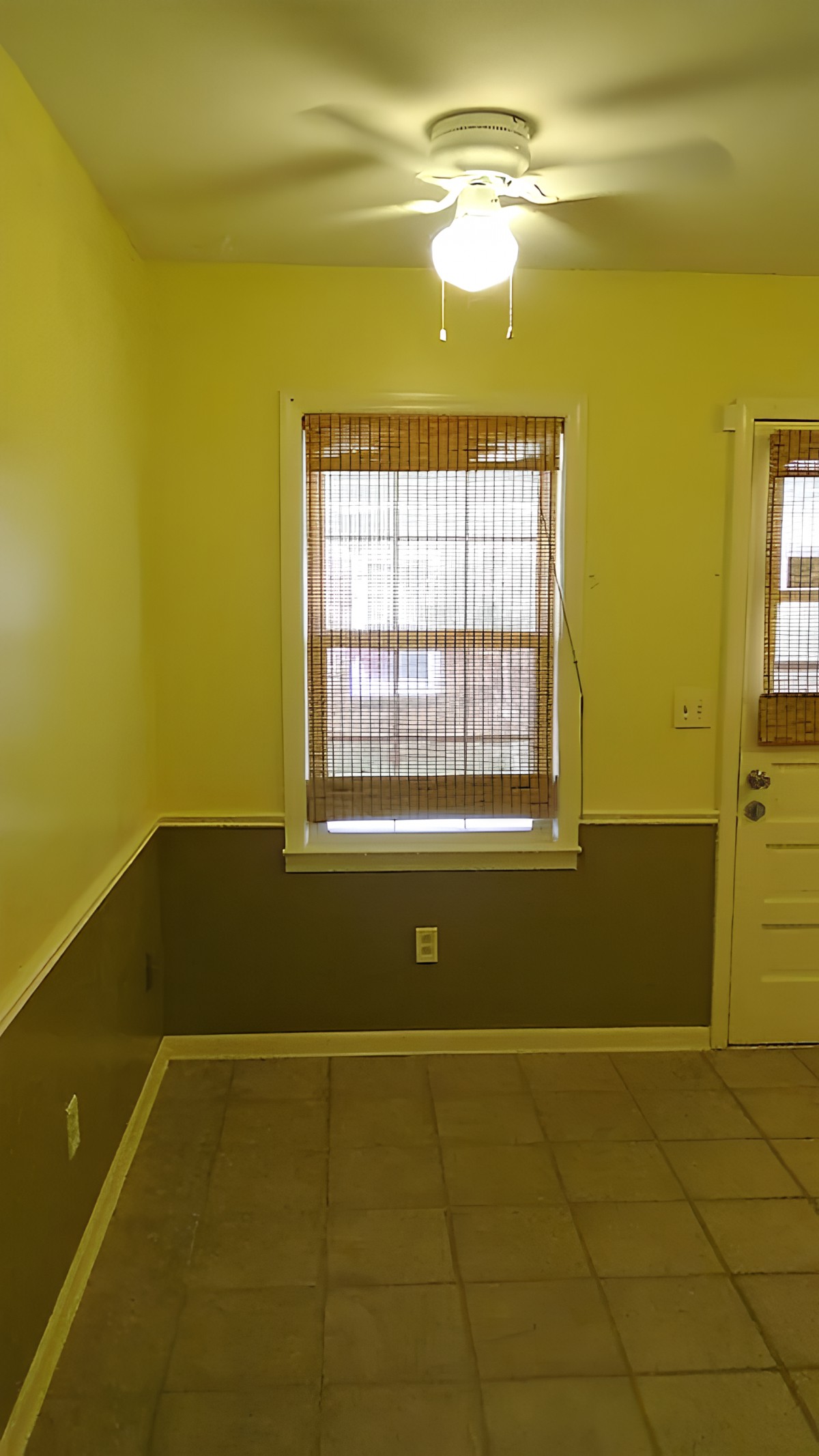 An empty room with green walls, a window with bamboo blinds, and a door.