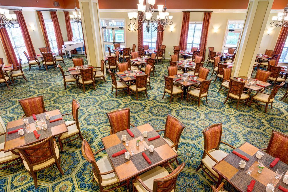 An elegant dining room with neatly arranged tables and chairs, featuring chandeliers and a carpeted floor.