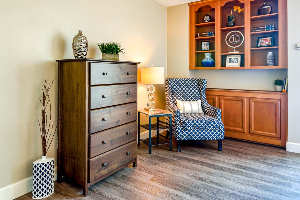 Cozy living room corner with a wooden dresser, patterned armchair, and warm lighting.