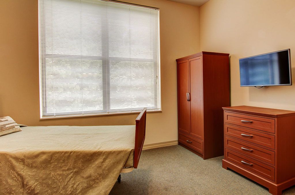 A minimalist bedroom with a bed, wardrobe, and dresser near a large window.