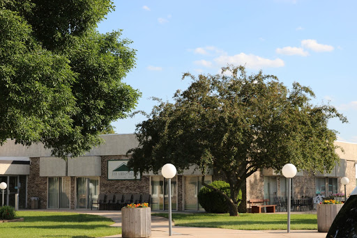 A serene view of a park area featuring a building, lush greenery, and decorative lighting.