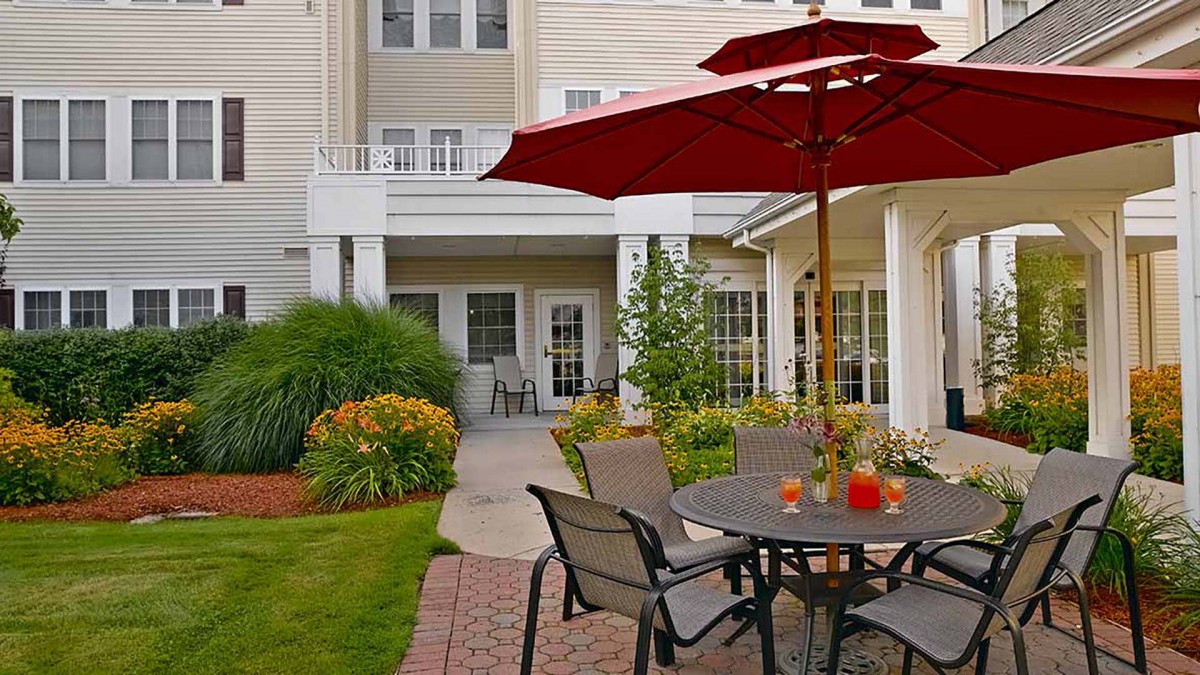 A cozy patio area with lawn chairs and a red umbrella, surrounded by a well-maintained garden.