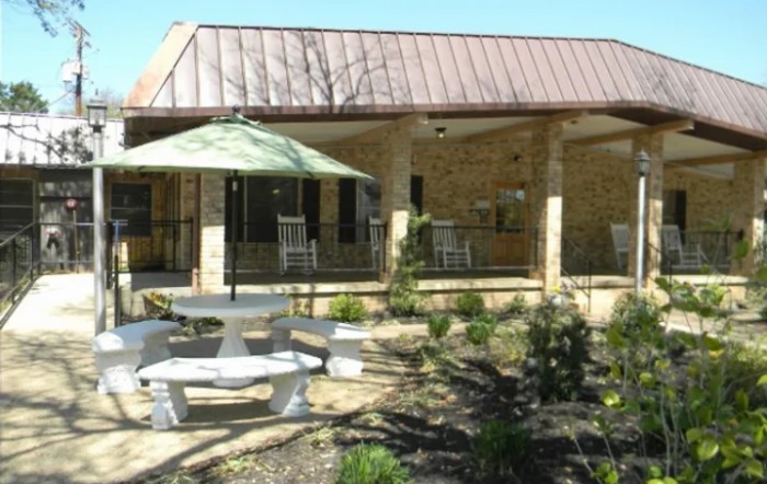An outdoor patio area with seating, featuring a table with an umbrella and surrounded by landscaping.