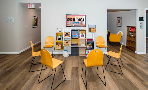 A cozy waiting area in a yoga studio featuring bright yellow chairs and an organized bookshelf.