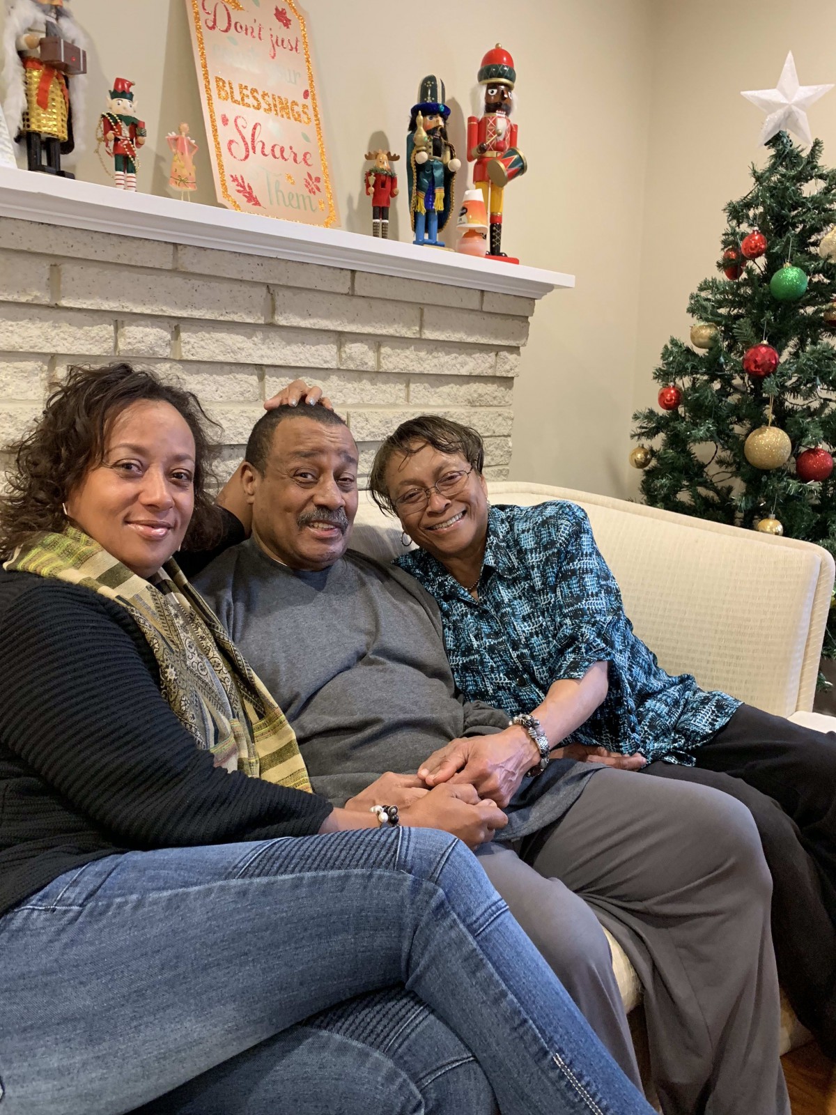 A family sitting together on a couch in a living room, celebrating the holidays with a decorated Christmas tree in the background.