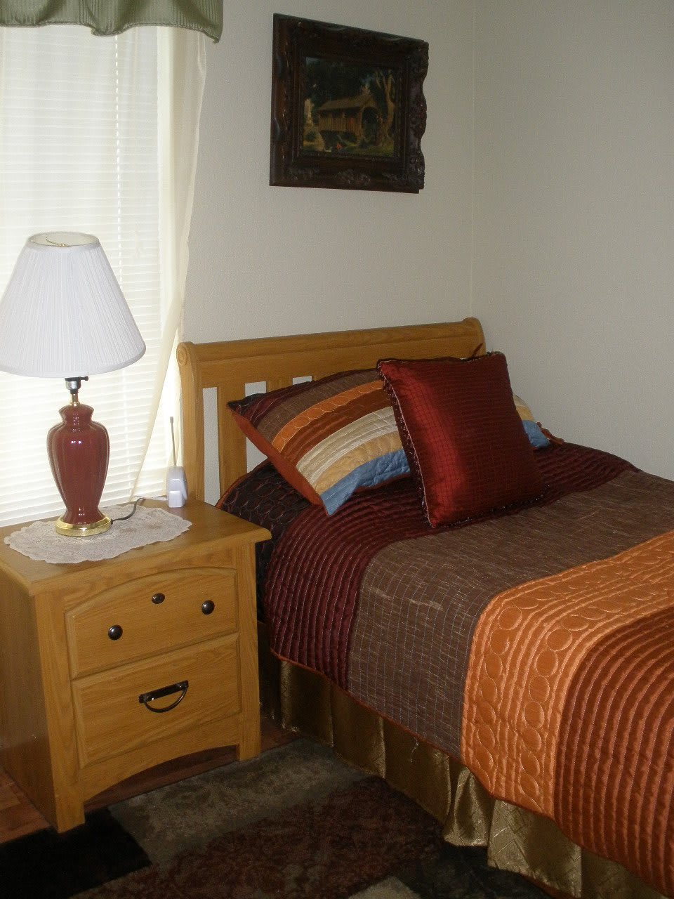 A cozy bedroom with a single bed, colorful pillows, and a lamp on the nightstand.