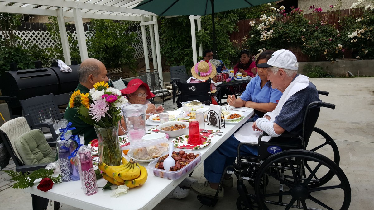 A family gathering around a table outdoors, enjoying food and conversation.