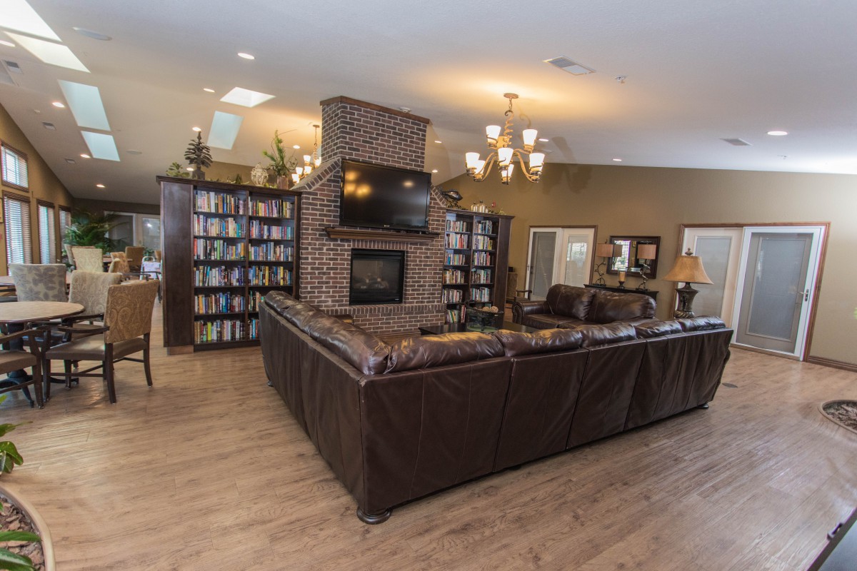 A cozy living room with a large leather sectional sofa, centered around a brick fireplace and television, flanked by bookshelves.