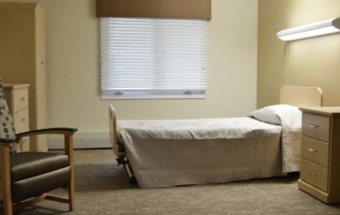 A minimalist bedroom with a single bed and a chair near a window.