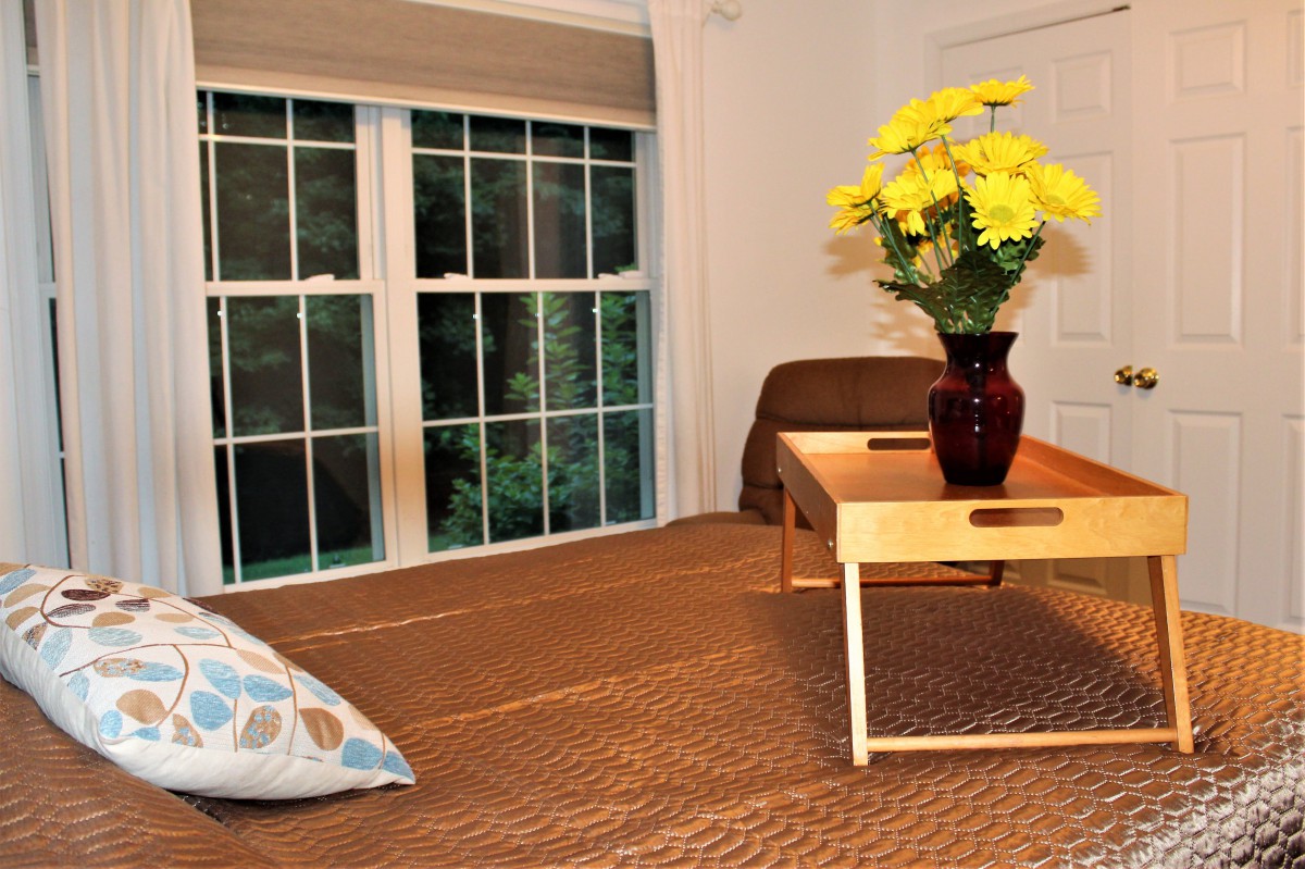 A cozy living room with a wooden table, vase of yellow flowers, and large window.