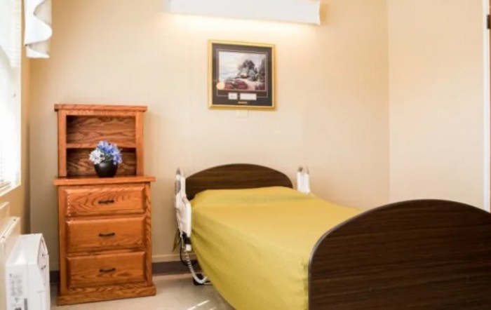 A hospital room with a single bed, wooden furniture, and decorative elements including a painting and flowers.