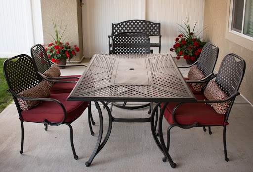 A stylish outdoor dining set featuring a decorative table and comfortable chairs with red cushions, complemented by vibrant flowers.