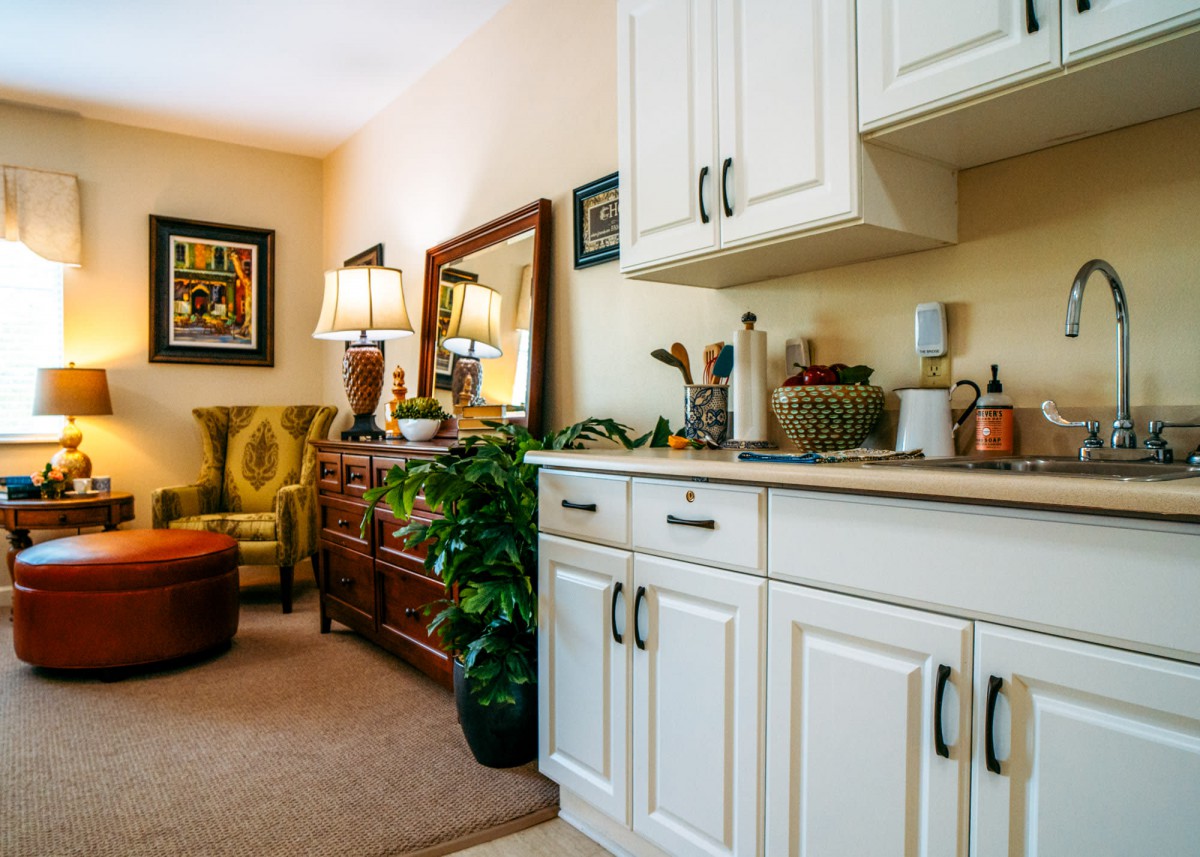 A cozy living room with white cabinets, a large mirror, plants, and comfortable seating.