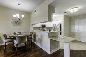 A modern kitchen and dining area with sleek furnishings, featuring a chandelier and wooden flooring.