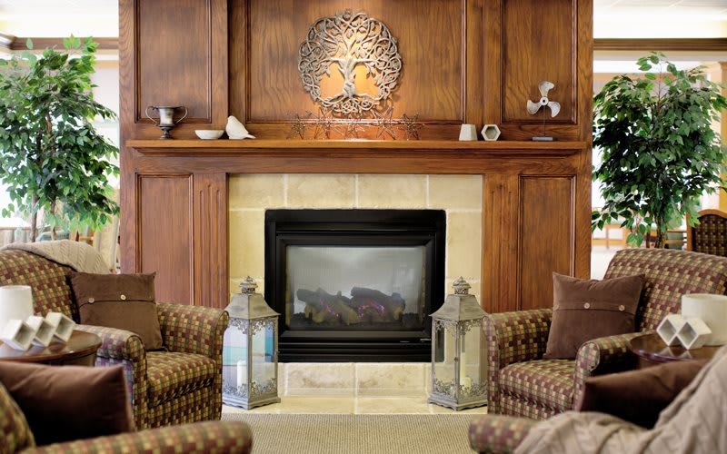 A cozy living room features a central fireplace surrounded by elegant wood paneling, with lanterns and plush armchairs adding to the inviting atmosphere.