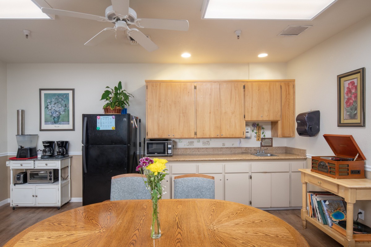 A cozy kitchen interior with wooden cabinets, a black refrigerator, and a round table decorated with fresh flowers.