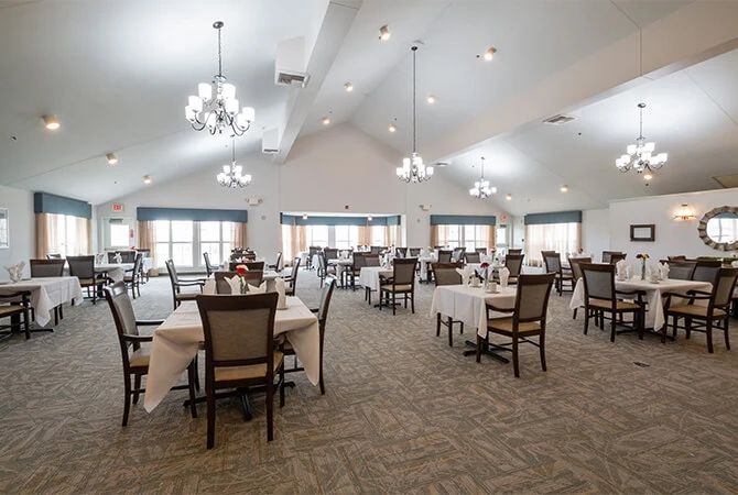 A spacious dining area with neatly arranged tables and chairs, illuminated by elegant chandeliers.
