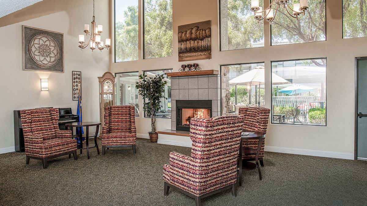 A cozy living room with armchairs and a fireplace, adorned with large windows and chandeliers.