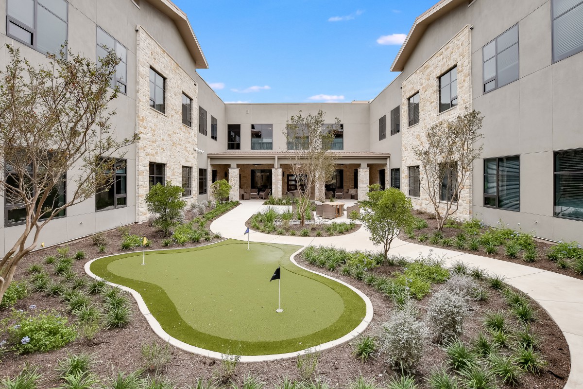 A landscaped courtyard featuring a small putting green surrounded by a two-story building.