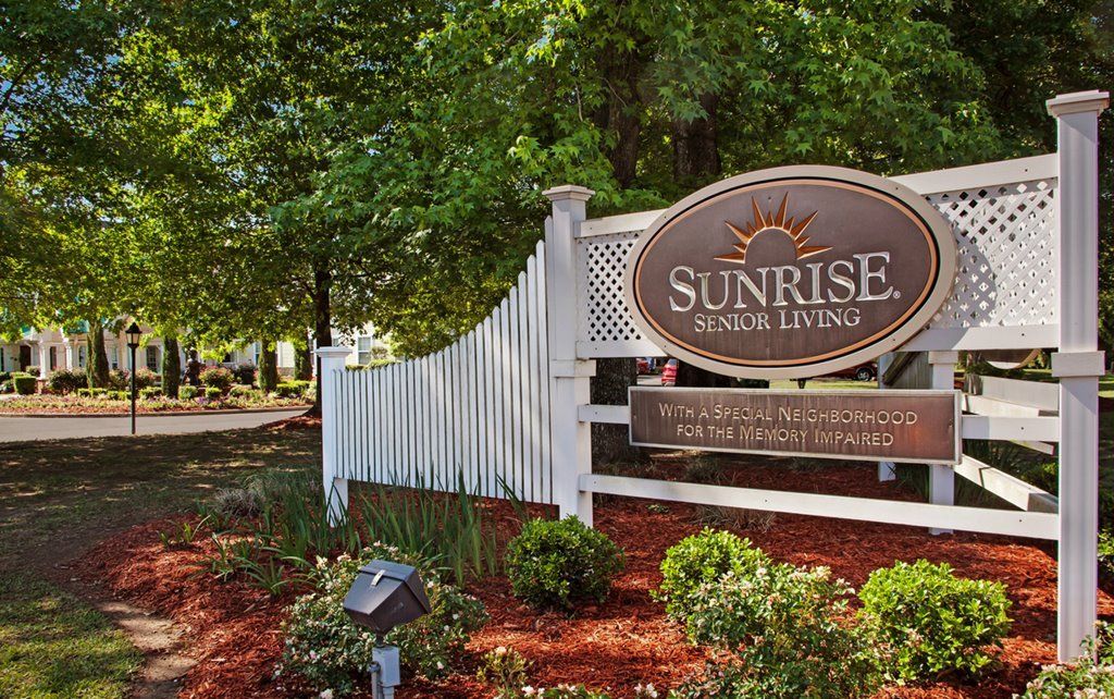 Entrance sign for Sunrise Senior Living surrounded by lush greenery.