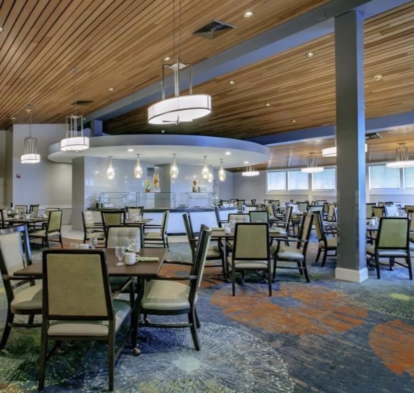 A modern restaurant interior with neatly arranged tables and chairs, illuminated by stylish ceiling lights.