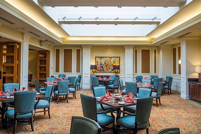 A well-lit dining room with multiple tables and chairs arranged under a large skylight.