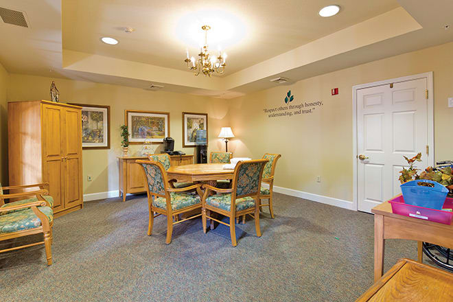 A well-lit meeting room with a round table and four chairs, decorated with artwork and a chandelier.