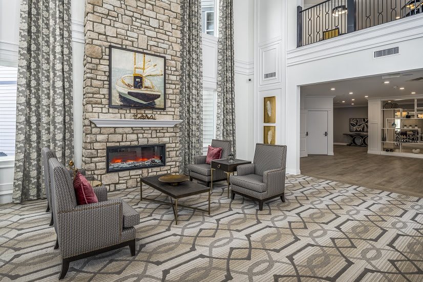 A modern living room featuring a stone fireplace, stylish armchairs, and a high ceiling.