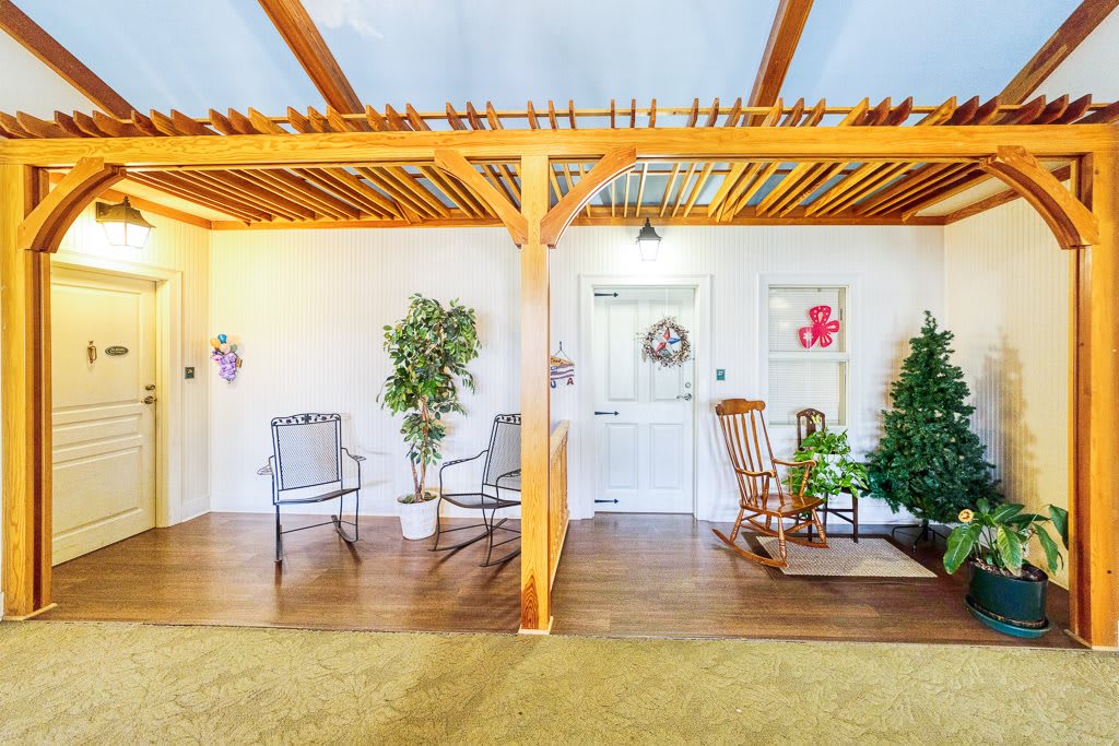 A cozy indoor space featuring a seating area with chairs and a rocking chair, wooden beams, and decorative plants.