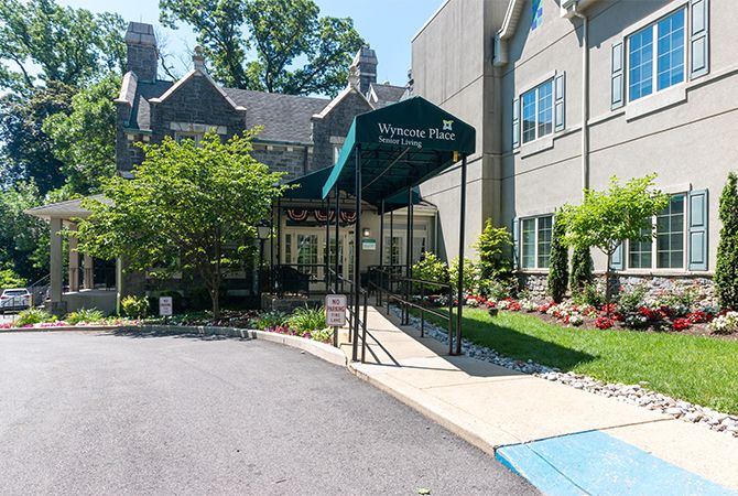 A welcoming entrance to a building with a green awning and well-maintained landscaping.
