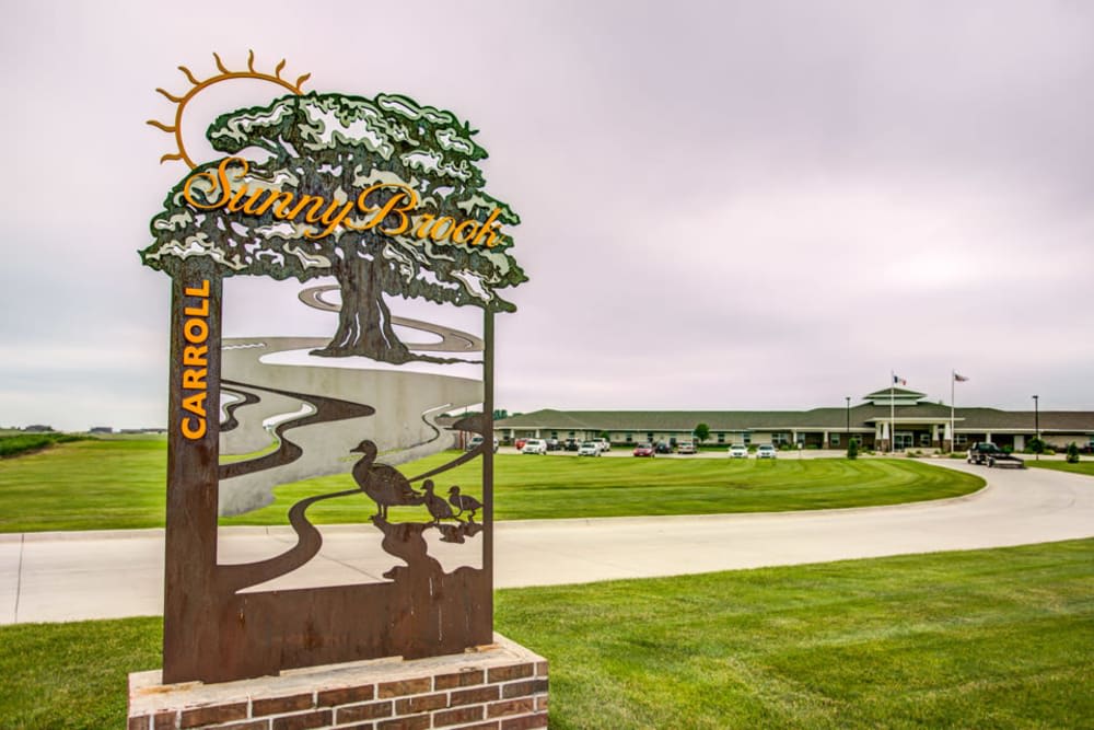 A scenic view of a park entrance with a decorative sign in the foreground and lush greenery surrounding the area.