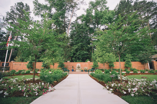 A serene garden pathway lined with lush trees and vibrant flower beds, inviting visitors into a peaceful outdoor space.